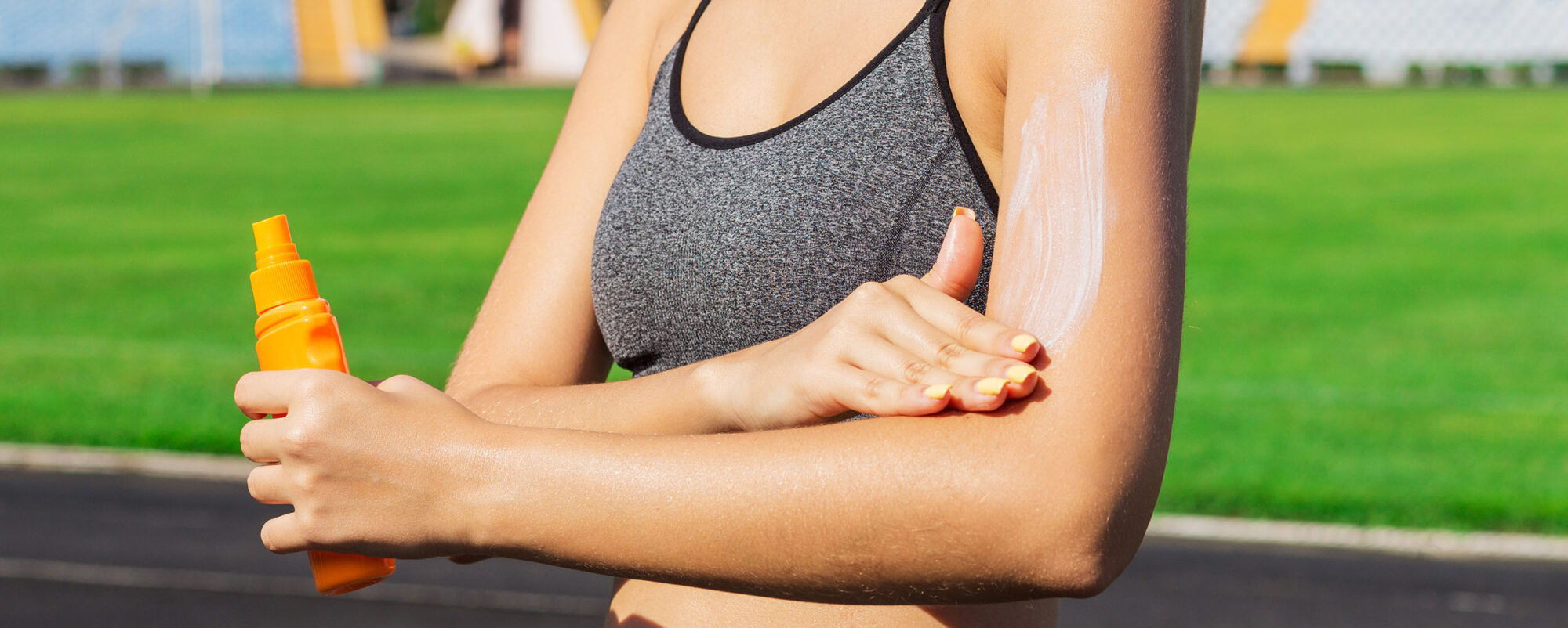Young Woman Is Applying Sunscreen On Her Arms Before Physical Activities At The Stadium. Protect Your Skin From Sunburn
