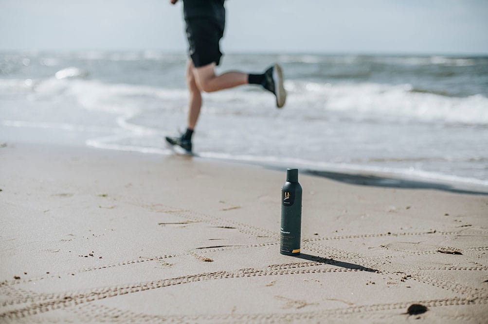 U-Sport Shoe Impregnator op het strand met hardloper op de achtergrond voor bescherming van sportschoenen