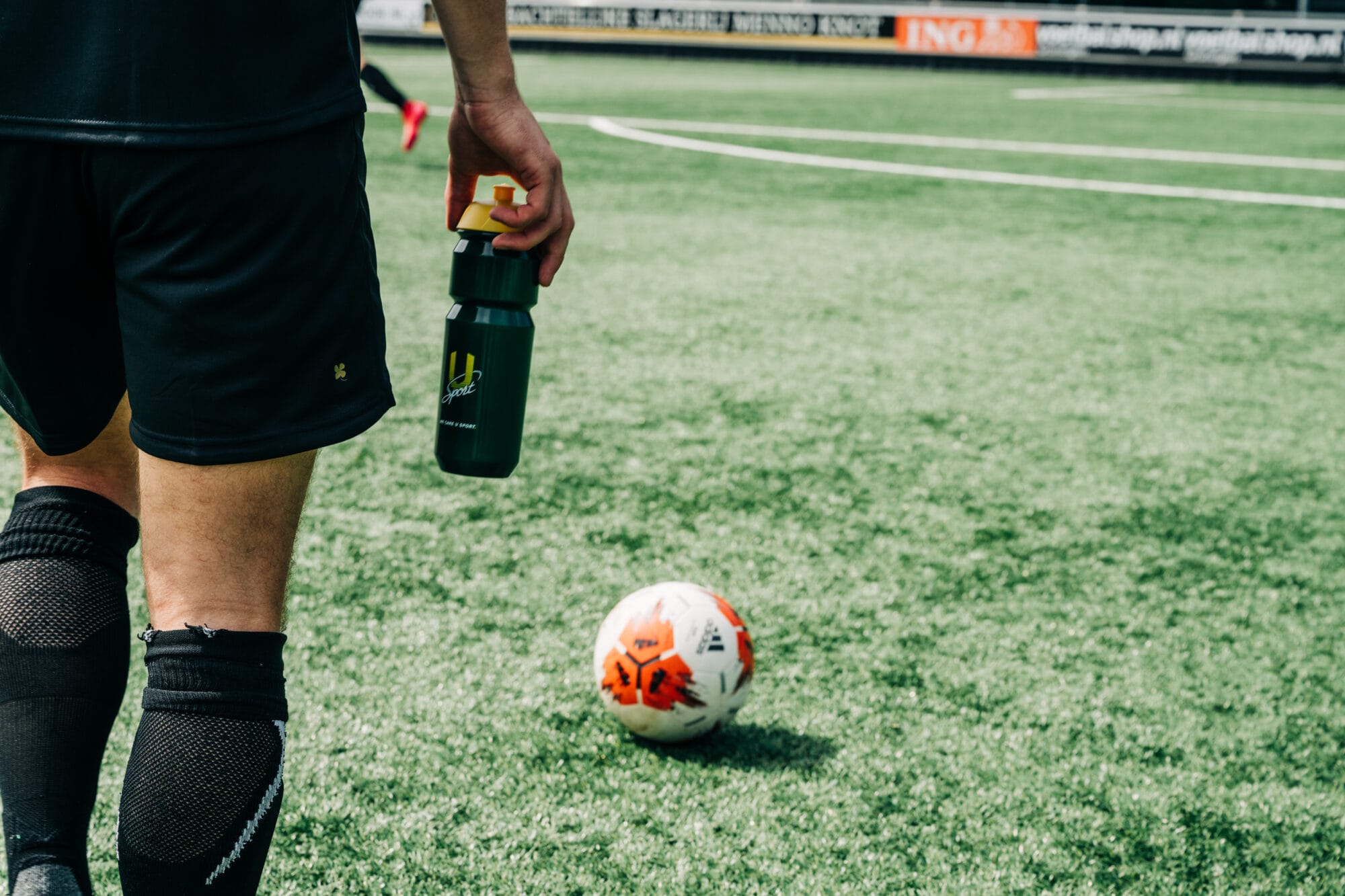 Voetballer met U-Sport Performance Sports Bottle op een voetbalveld