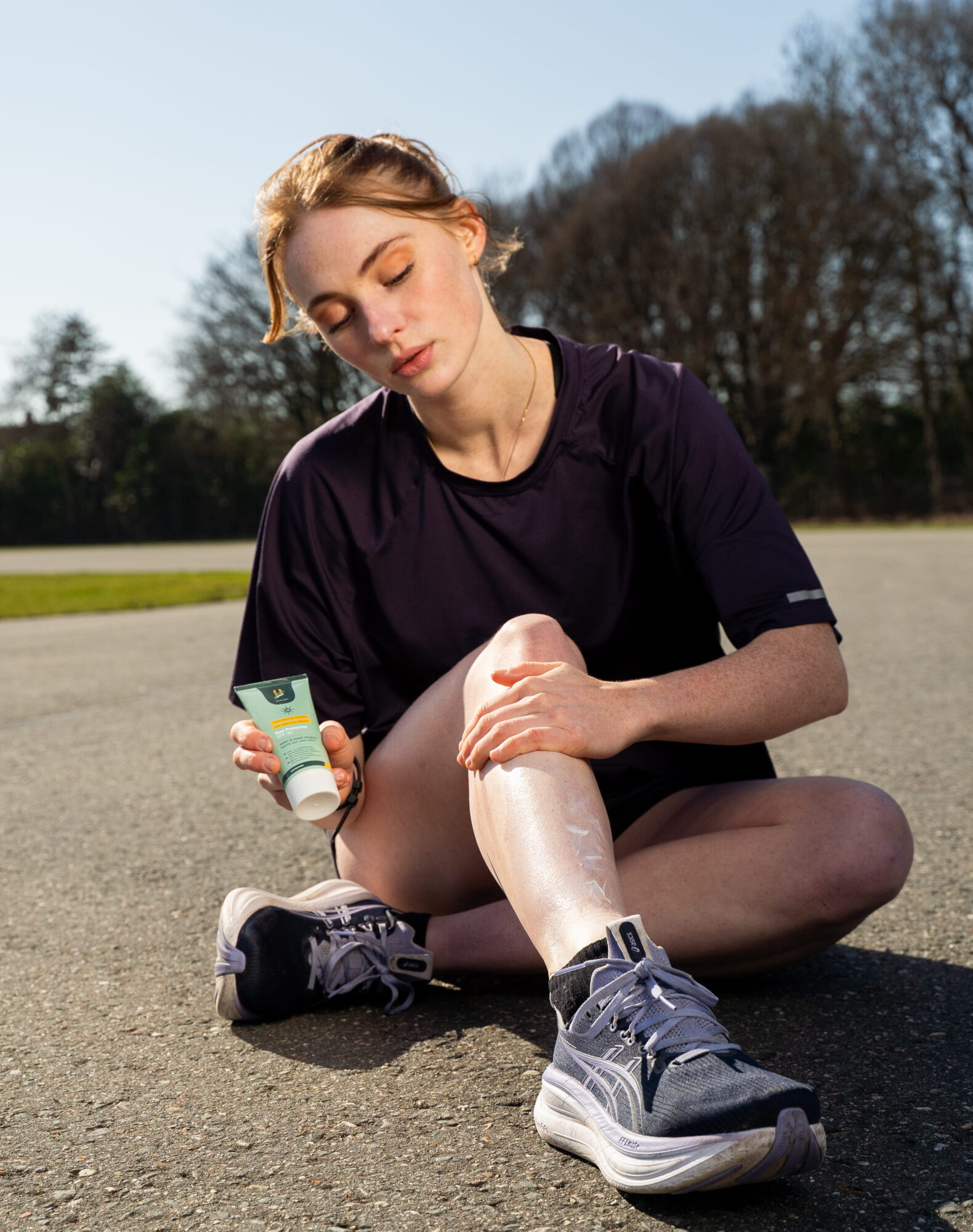 Hardloper smeert zweetbestendige zonnebrandcrème SPF 30 op haar been voor een buitentraining.